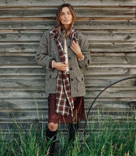 Model showcasing stylish Knitwear with a plaid scarf against a rustic wooden backdrop.